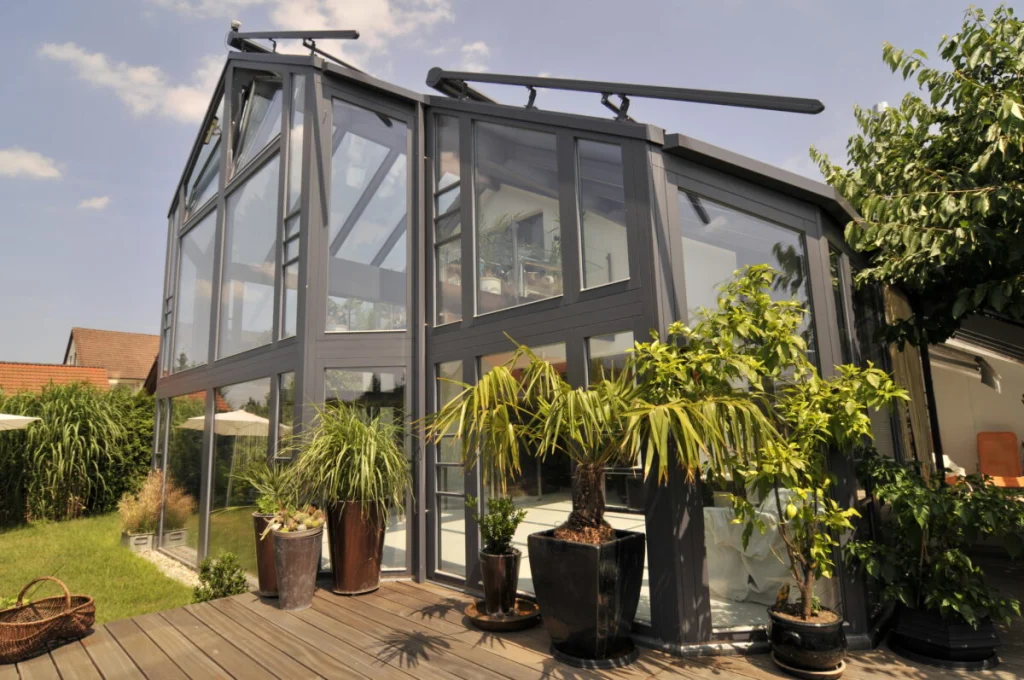 Zweigeschossiger Wintergarten in Baiersdorf mit anthrazitfarbenen Rahmen und verglastem Satteldach, Holzdeck mit Kübeln
