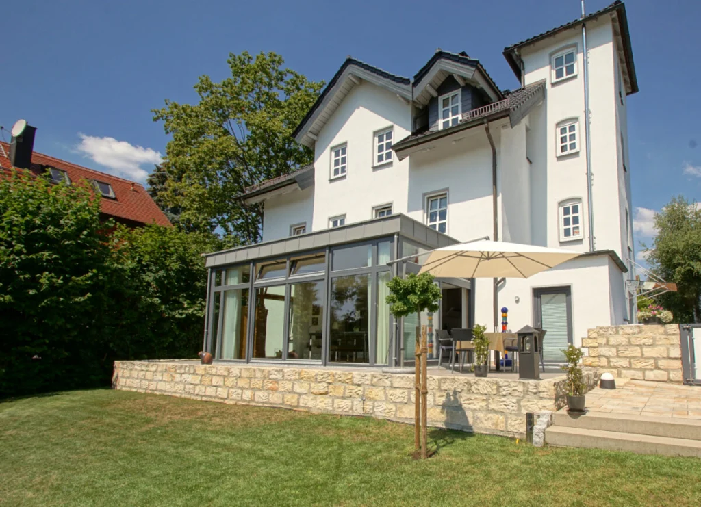 Villa in Coburg mit Flachdach-Anbau als Esszimmer, anthrazitfarbene Rahmen, Terrasse auf Sandsteinmauer