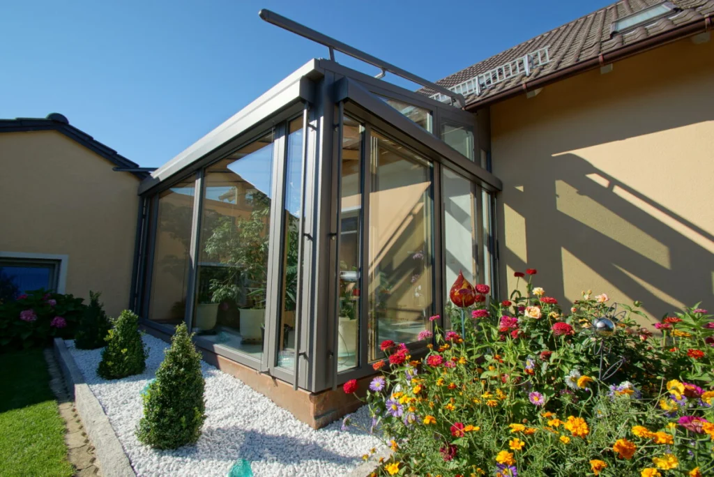 Pultdach-Wintergarten in Ebensfeld mit grauer Aluminiumschale, Kiesbeet und Blumen vor beigem Haus