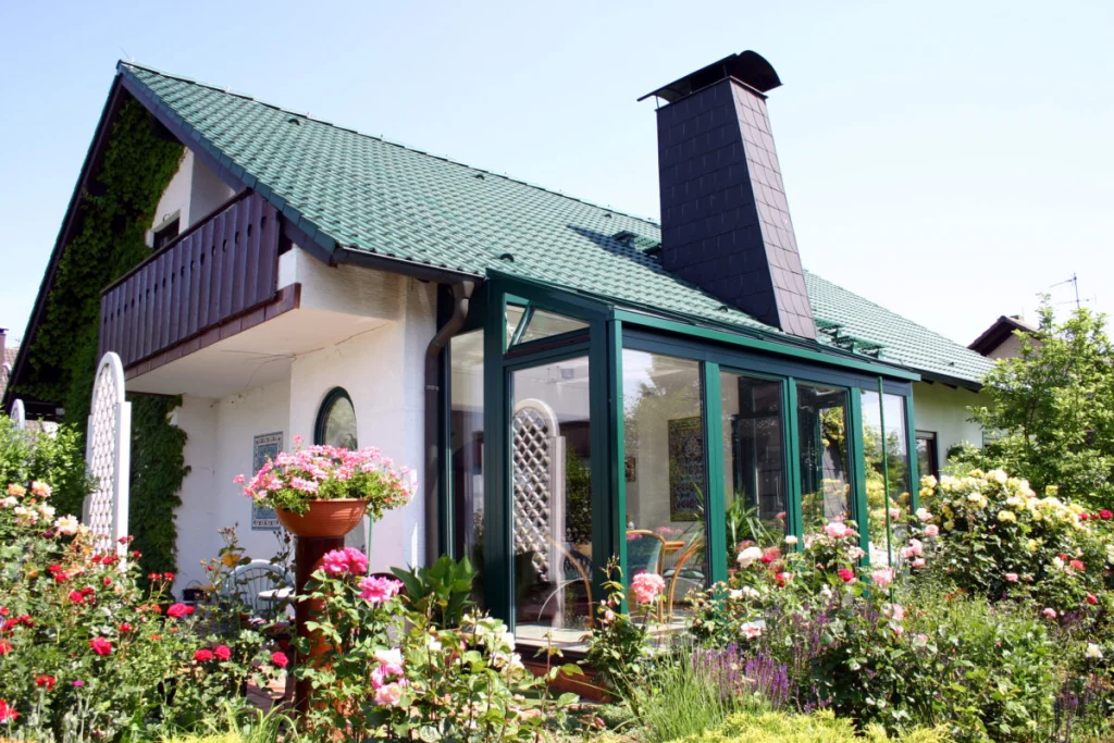 Haus in Effeltrich mit Holzbalkon, grünem Ziegeldach und Wintergarten mit dunkelgrünen Rahmen im Rosengarten