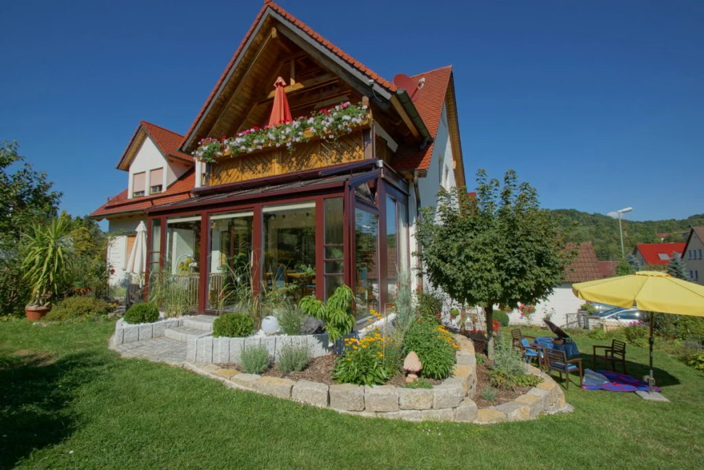 Wintergarten in Heiligenstadt mit dunkelroten Holz-Alu-Profilen unter dem Balkon, Blick über Rasen und Steinbeet