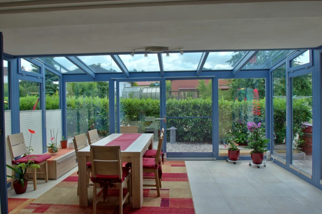 Wintergarten in Herpersdorf mit Pultdach aus Glas, blaugrauen Profilen, Esstisch und Blick auf Hecke und Garten