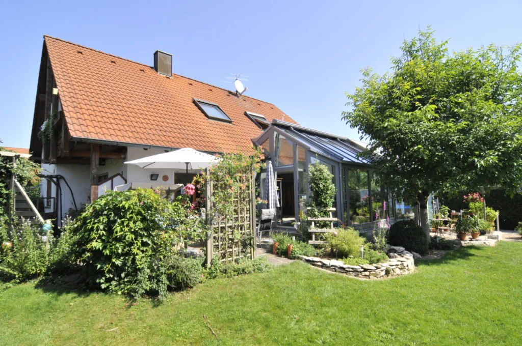 Einfamilienhaus in Kleinsendelbach mit grauem Pultdach-Wintergarten an der Traufseite, Garten mit Baum und Pergola