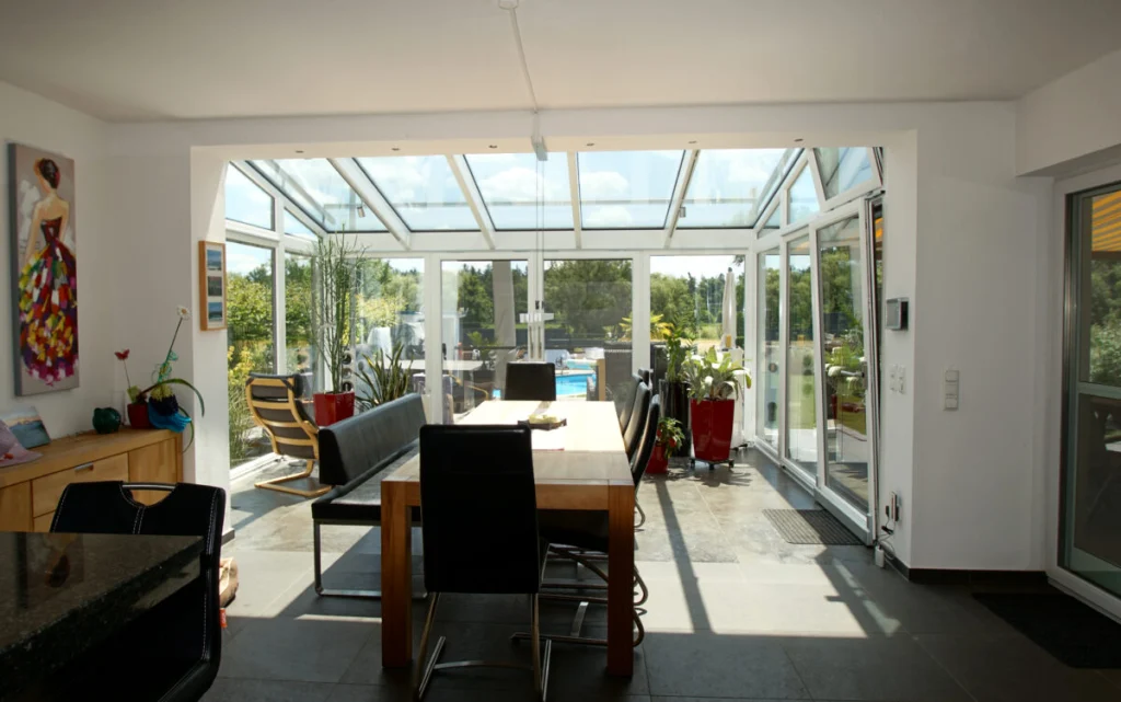 Wintergarten in Königsfeld als Esszimmer mit Glasdach, weißen Profilen und Blick auf Terrasse und Pool