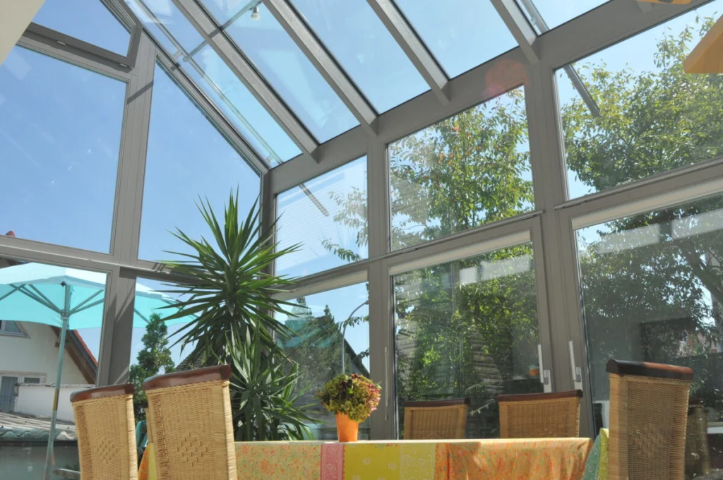 Wintergarten in Leutenbach von innen, graue Profile, Glasdach über zwei Geschosse, Esstisch mit Rattanstühlen
