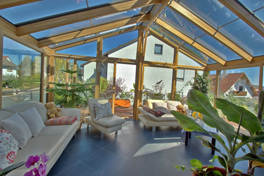 Wintergarten in Neudrossenfeld von innen mit Holzsparren, Glasgiebel, weißen Ledersofas und Blick auf die Terrasse