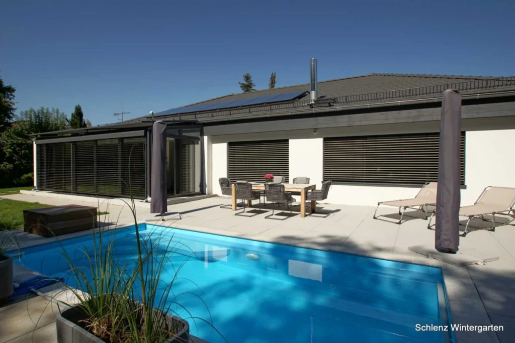 Wintergarten in Rathsberg an einem Bungalow mit Pool, anthrazitfarbene Rahmen, Raffstores geschlossen, Terrasse mit Essplatz