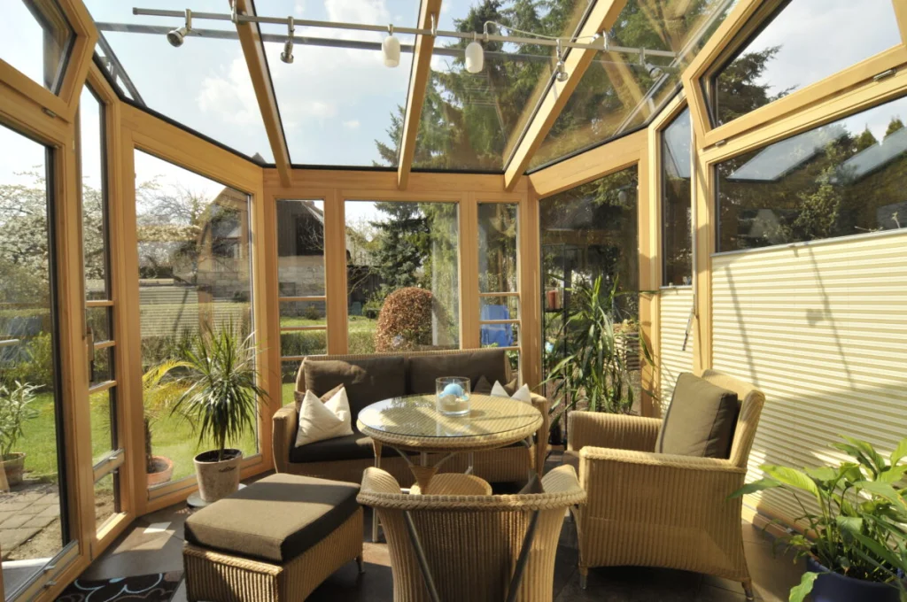 Wintergarten in Buch innen, Holzkonstruktion aus Meranti mit Glasdach, Rattanmöbel und Blick in den Garten