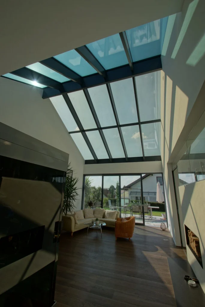 Glassatteldach in Buckenreuth von innen, hoher Wohnraum mit dunklen Sparren, Sofa und Schiebetür zum Garten