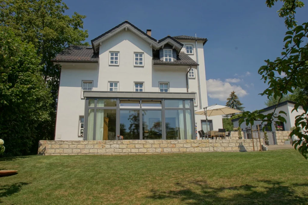 Weiße Villa in Coburg mit verglastem Flachdach-Anbau im Erdgeschoss, vom Garten gesehen