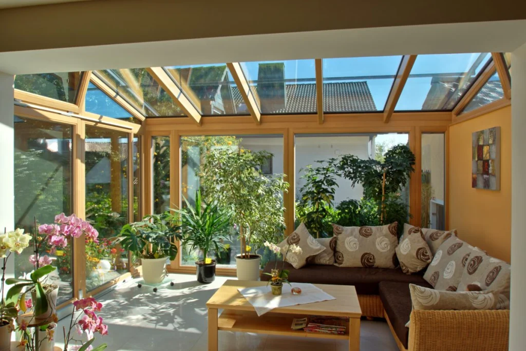 Wintergarten in Ebensfeld von innen mit Glasdach, Holzrahmen natur, brauner Eckcouch und Pflanzen