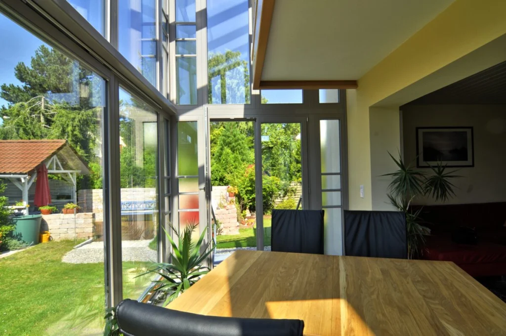Wintergarten in Hannberg, Esstisch aus Massivholz vor der zweigeschossigen Verglasung mit Blick auf Garten und Pavillon