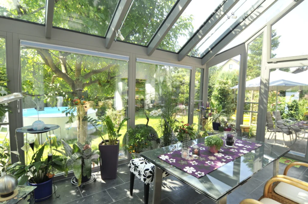 Wintergarten in Kleinsendelbach von innen mit grauen Profilen, Glasdach, Glastisch, Pflanzen und Blick auf den Garten