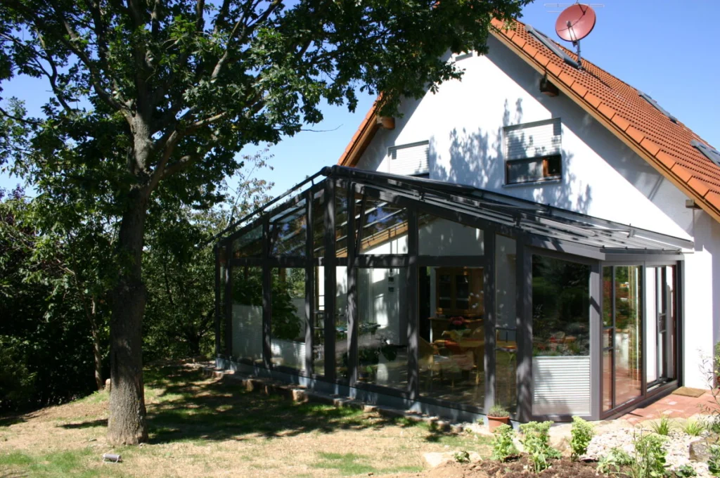 Wintergarten in Kunreuth mit Satteldach in Anthrazit am weißen Haus, Glasgiebel unter einem Baum, Blick in den Essplatz