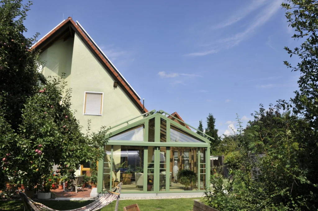 Wintergarten in Lauf mit grünem Satteldach am Giebel des hellgrünen Hauses, Garten mit Apfelbaum und Hängematte