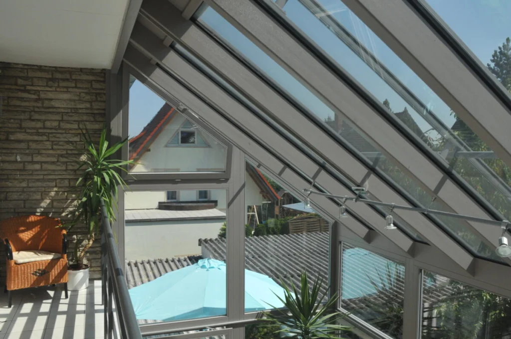 Obergeschoss des Wintergartens in Leutenbach, Loggia mit Natursteinwand, Rattansessel und Glasdach mit Beschattung