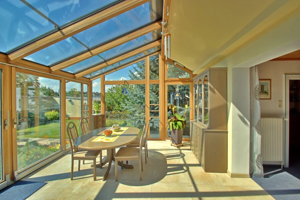 Wintergarten in Maiach von innen, Holzsparren und Glasdach, geschlossener Dachteil am Haus, ovaler Esstisch