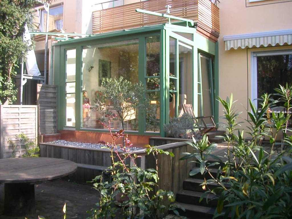 Kleiner Wintergarten in Schoppershof mit grünen Rahmen unter dem Balkon eines Reihenhauses, Blick vom Garten