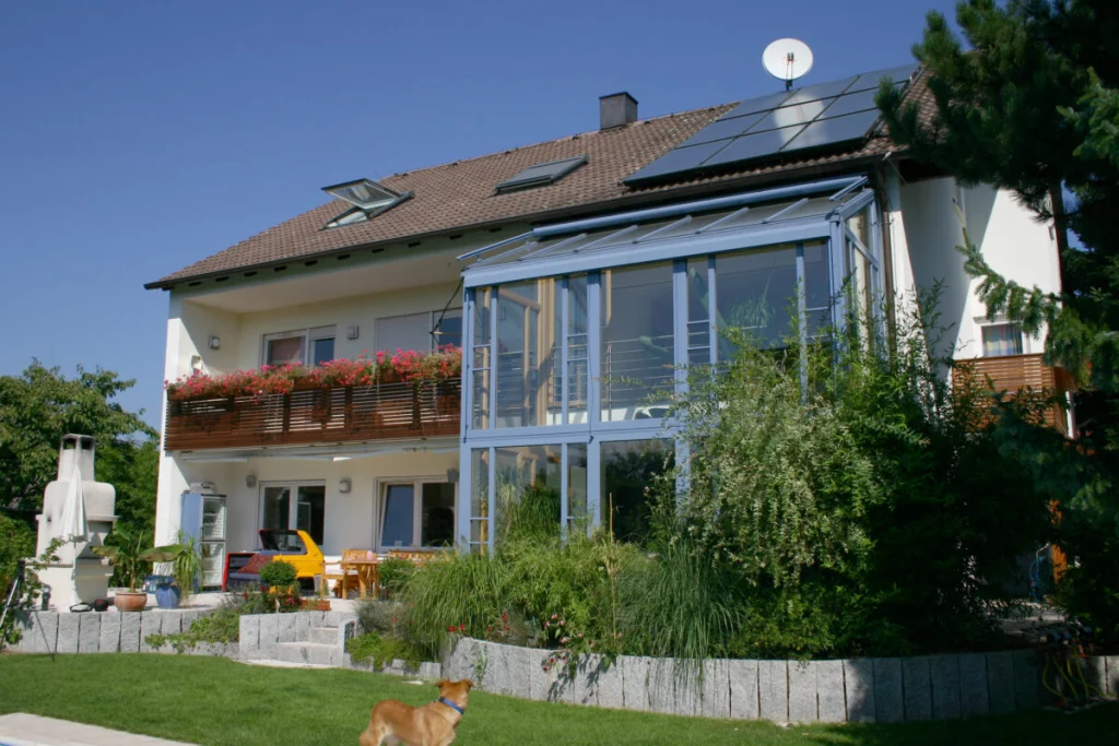 Haus in Bubenreuth mit zweigeschossigem Wintergarten in Blaugrau, Balkon mit Geranien und Solaranlage