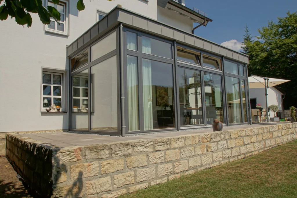 Flachdach-Anbau in Coburg mit anthrazitfarbenen Rahmen und Metallattika über einer Sandsteinmauer