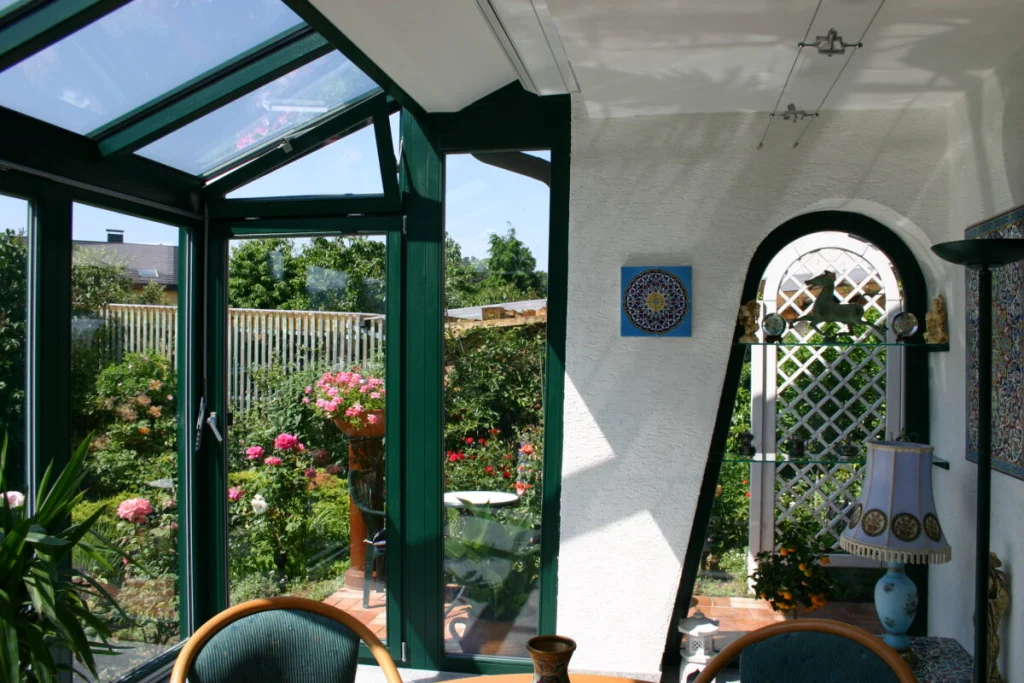 Wintergarten in Effeltrich innen mit dunkelgrünen Rahmen, Glasdach und offener Tür in den Rosengarten