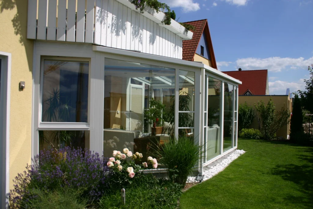 Wintergarten in Hausen von der Gartenseite, weiße Konstruktion unter dem Balkon, Lavendel und Rosen davor