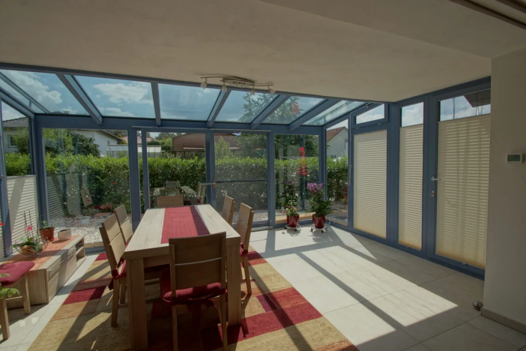 Wintergarten in Herpersdorf vom Wohnraum aus, Glasdach mit blaugrauen Profilen, Esstisch und Plisseestores