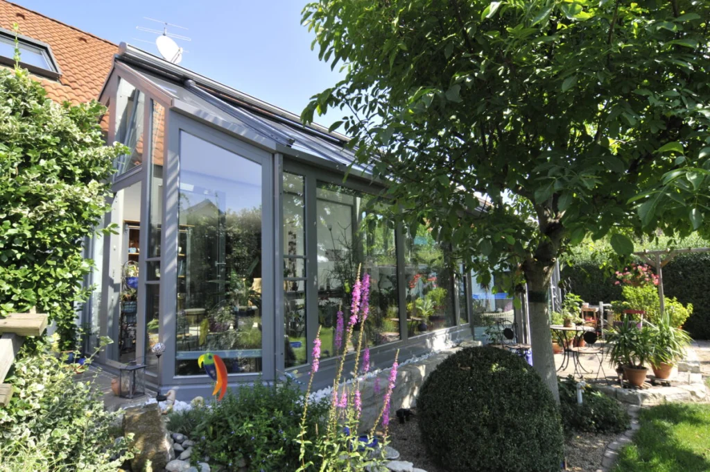 Wintergarten in Kleinsendelbach mit grauen Profilen und Pultdach, geschlossener Dachteil am Haus, Garten mit Baum