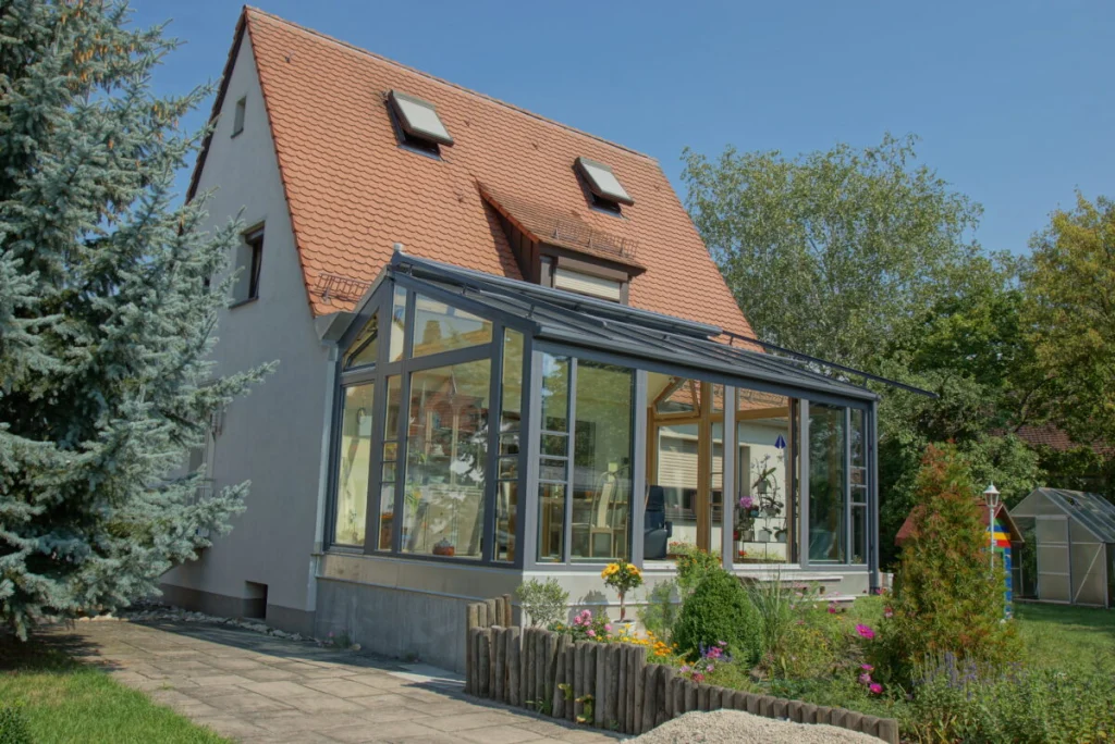 Einfamilienhaus in Maiach mit anthrazitfarbenem Pultdach-Wintergarten an der Giebelseite, Garten mit Blumenbeet
