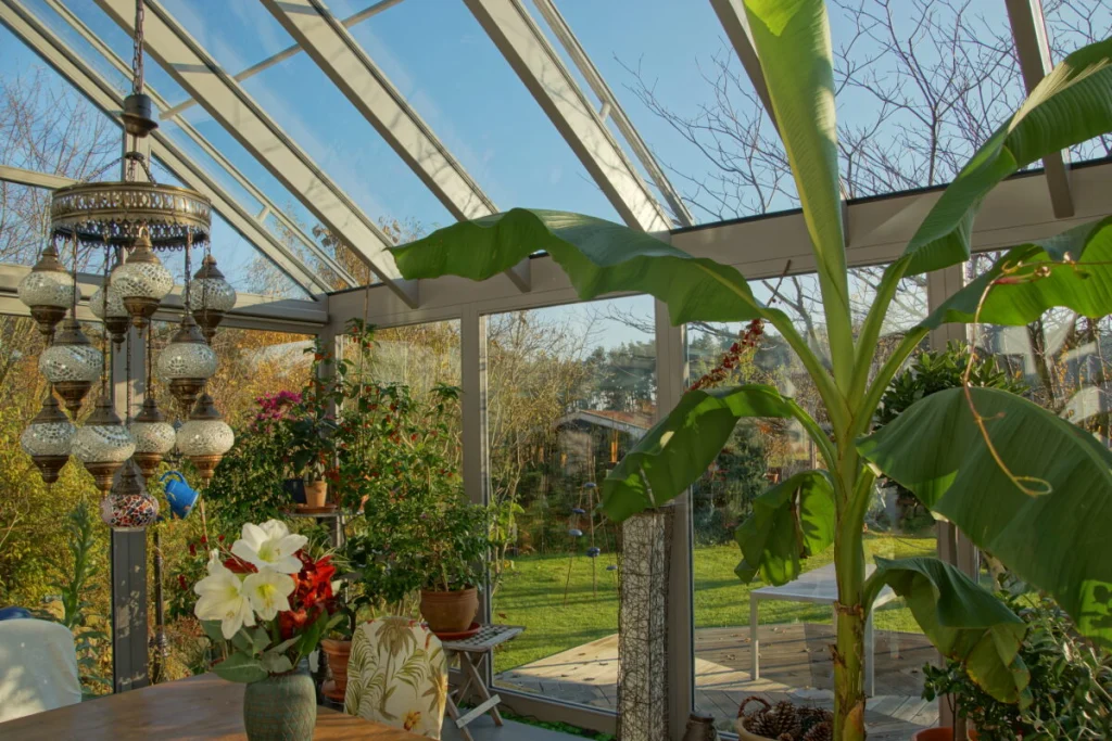 Wintergarten in Möhrendorf von innen mit Bananenstaude, Mosaikleuchte, Glasdach und Blick auf Rasen und Holzdeck