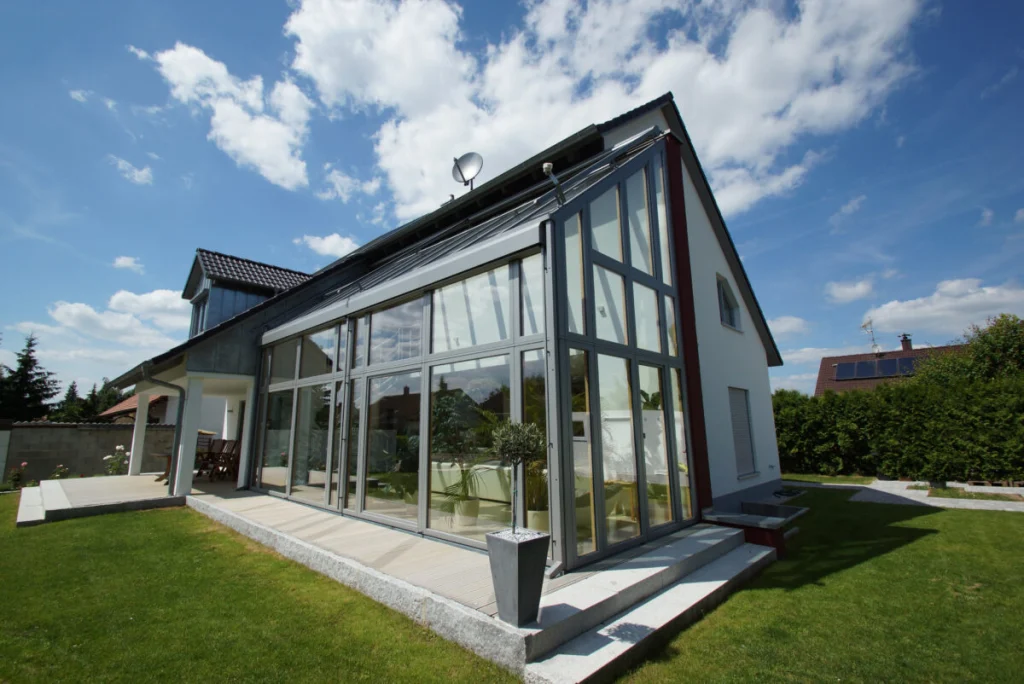 Zweigeschossiger Glasanbau in Bruck mit hellgrauen Aluminiumrahmen und Glasdach, Holzdeck mit Olivenbaum, von unten