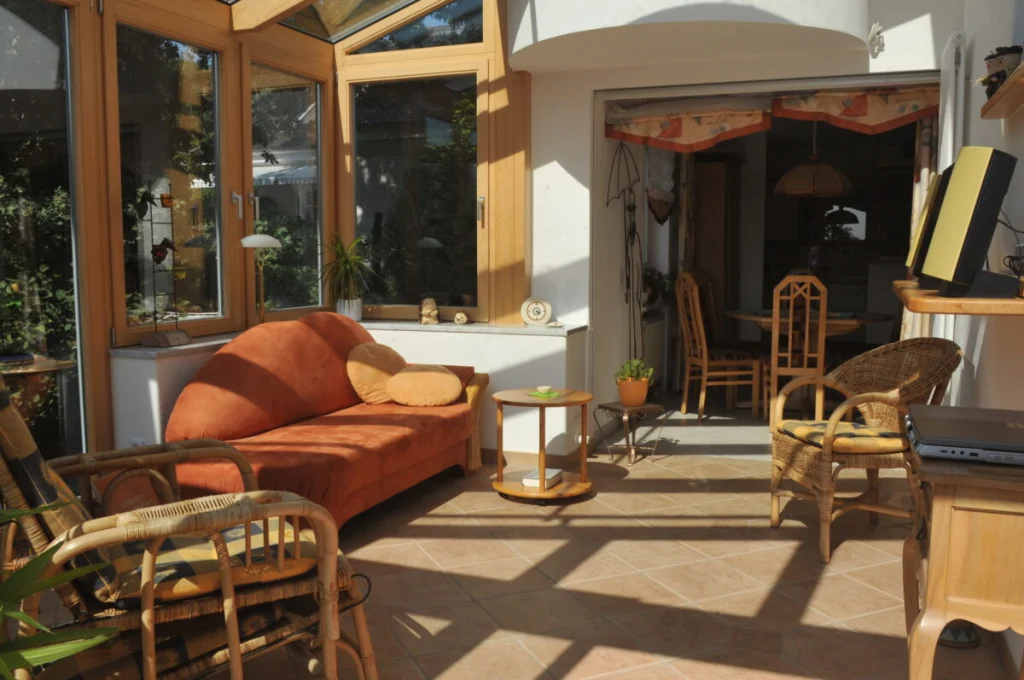Sitzecke im Wohnwintergarten in Buckenhofen mit orangefarbenem Sofa, Rattansesseln und Terracottafliesen