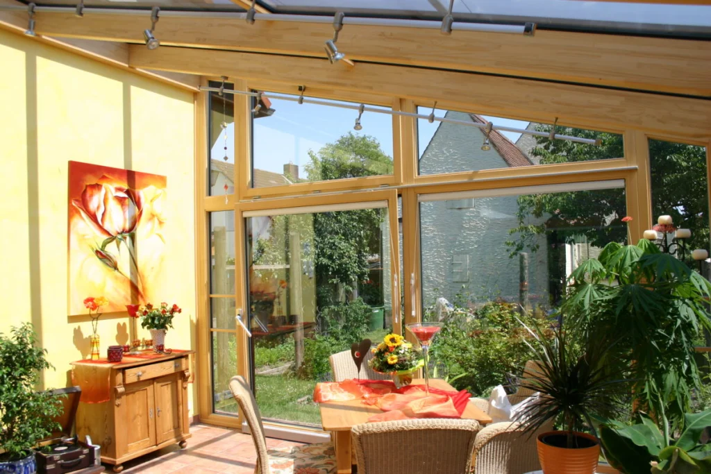 Wintergarten in Dechsendorf innen mit gelber Wand, Rosenbild, Holzkommode und Fensterfront zum Garten