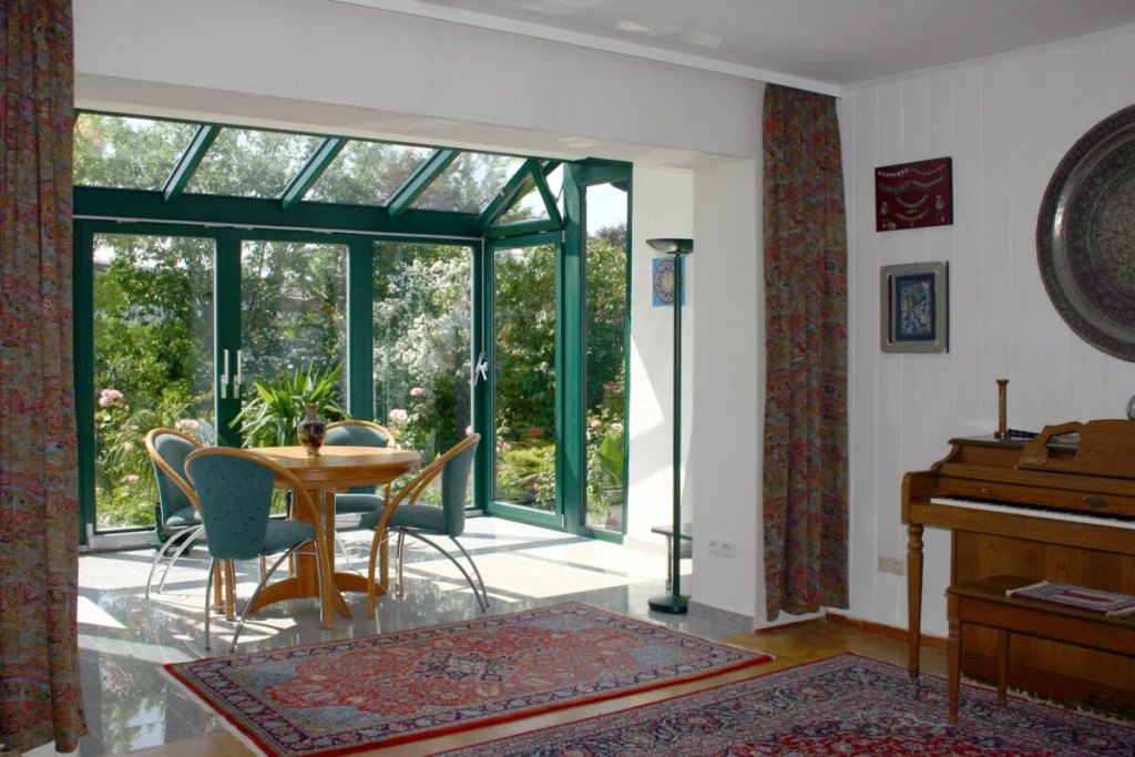 Blick aus dem Wohnzimmer in den Wintergarten in Effeltrich mit grünen Rahmen, Glasdach und rundem Esstisch