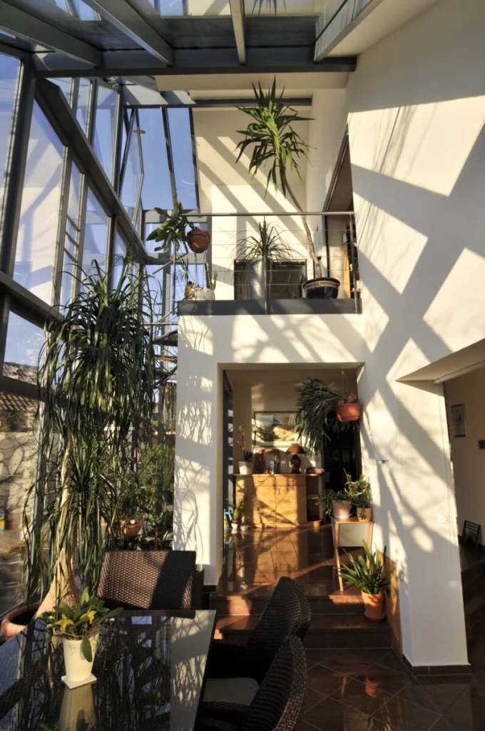 Dreigeschossiger Glasvorbau in Fürth von innen mit Galerie, Glasdach, Pflanzen und Essplatz