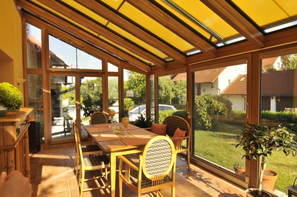 Wintergarten in Großenbuch innen mit ausgefahrener gelber Markise über dem Glasdach und Blick in den Garten