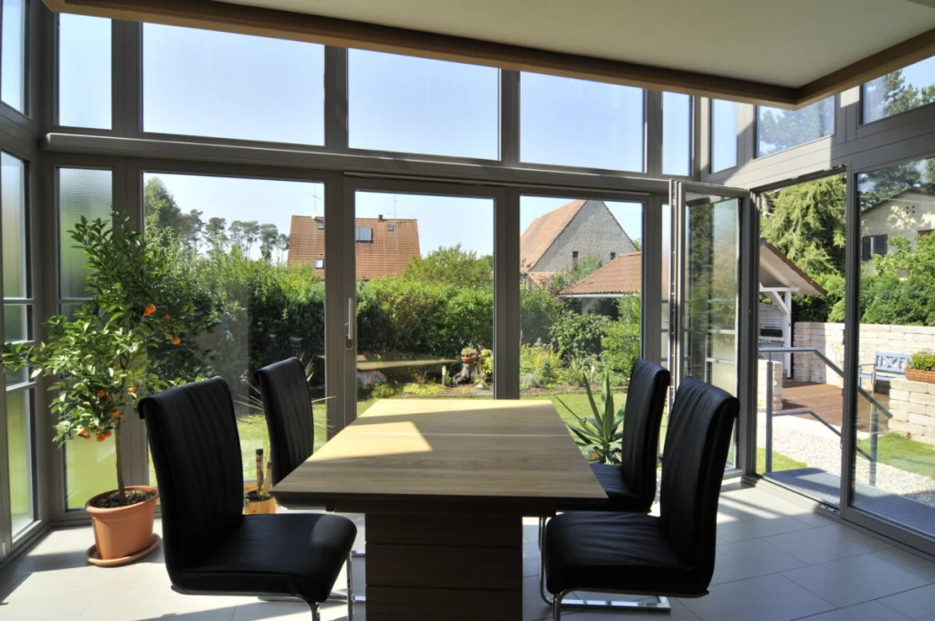 Wintergarten in Hannberg mit Esstisch, offener Flügeltür und Blick auf Garten, Holzterrasse und Nachbarhäuser