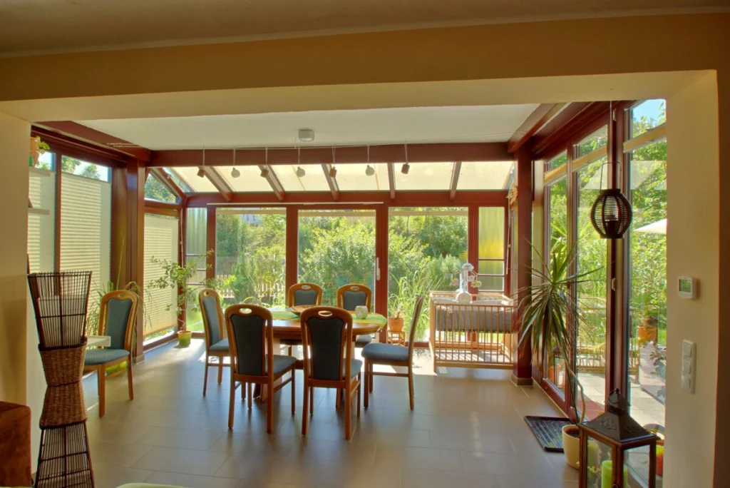 Wintergarten in Heiligenstadt vom Wohnraum aus, dunkelrote Profile, Glasdach und Esstisch mit Blick in den Garten