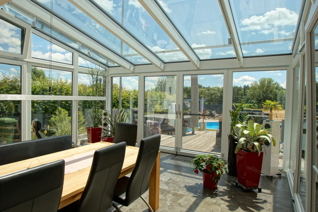 Wintergarten in Königsfeld, Blick unter dem Glasdach zur offenen Doppeltür mit Holzterrasse und Pool dahinter