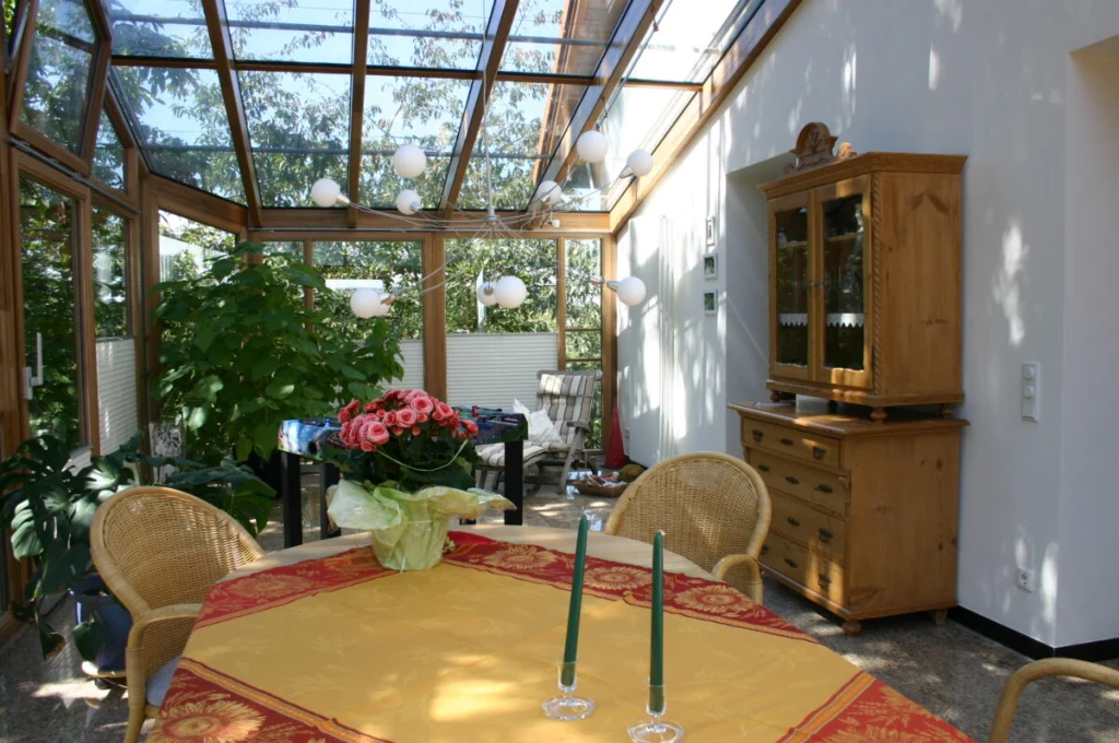 Wintergarten in Kunreuth von innen, Holzsparren, Glasdach, Bauernschrank und Esstisch mit Rattanstühlen