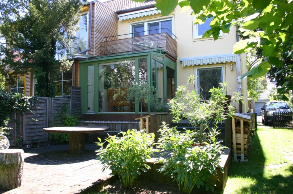 Reihenhaus in Schoppershof mit Holzfassade, Balkon und kleinem Wintergarten mit grünen Rahmen im Sommer