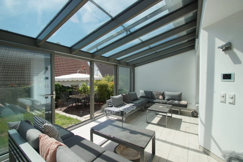 Wintergarten in Baunach mit Loungemöbeln unter dem Glasdach und offener Schiebetür zum Garten