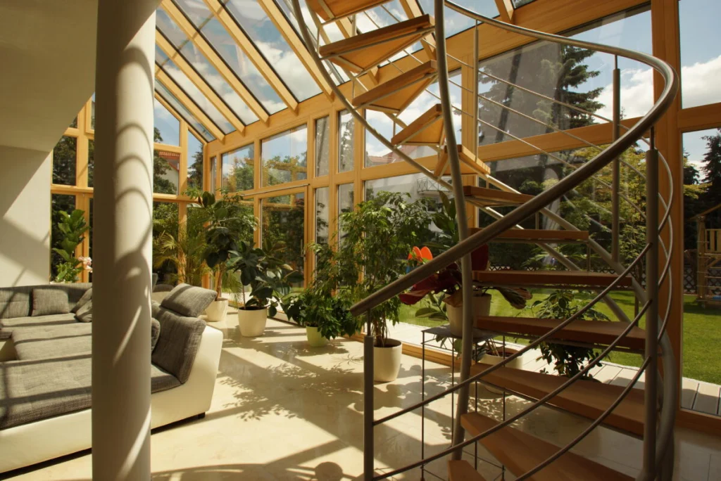 Wendeltreppe aus Stahl mit Holzstufen im Glasanbau in Bruck, Glasdach mit Holzsparren, Sofa und Pflanzen