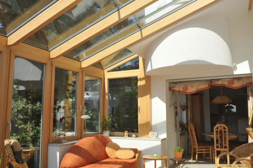 Wohnwintergarten in Buckenhofen von innen mit Glasdach, Holzsparren natur, orangefarbenem Sofa und Durchgang zur Küche