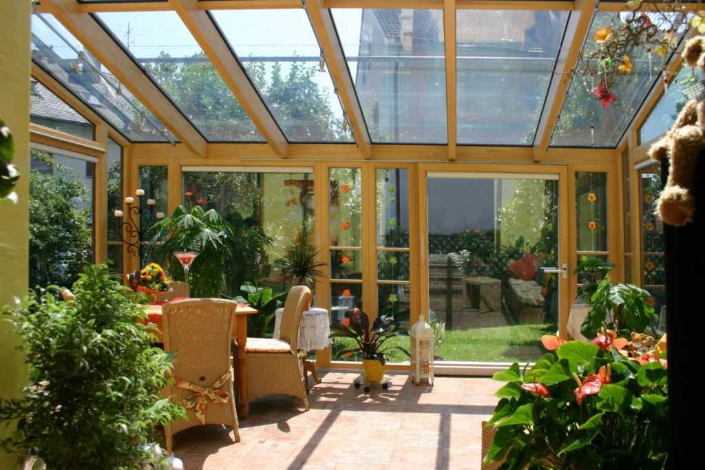 Wintergarten in Dechsendorf von innen mit Glasdach, Holzrahmen natur, Rattanstühlen und Blick in den Garten
