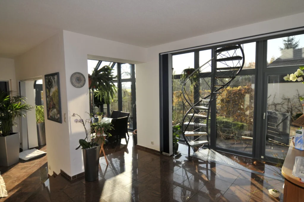 Wohnraum im Glasvorbau in Fürth mit anthrazitfarbenen Rahmen, Wendeltreppe und dunklen Fliesen