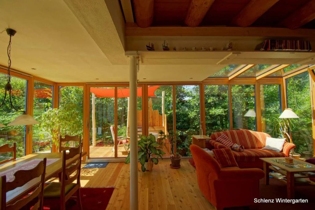 Anbau in Grafenau innen mit Blick auf die Terrasse und das rote Sonnensegel, rotes Sofa, Glaselemente im Dach