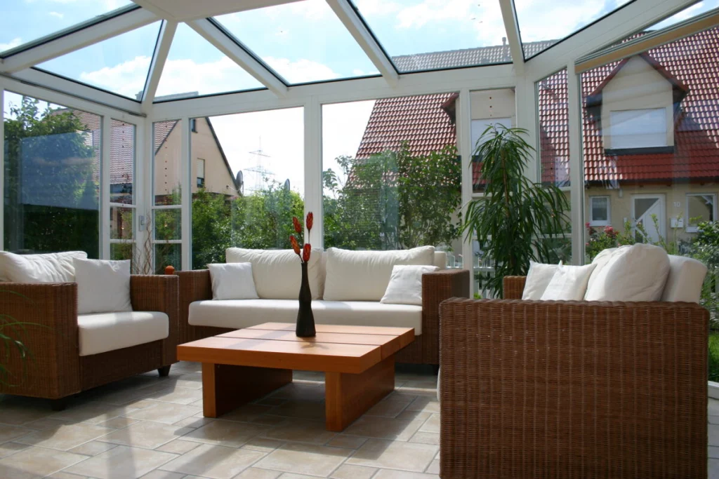 Wintergarten in Hausen von innen mit weißem Glasdach und Rattansofas, Blick auf Nachbarhäuser