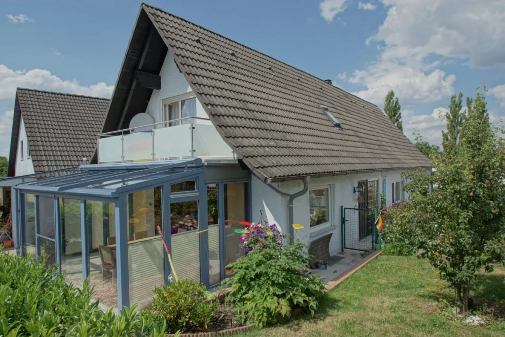Wintergarten in Herpersdorf an einem weißen Haus mit Satteldach, Außenansicht vom Garten mit Rasen und Sträuchern