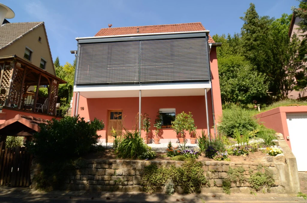 Rotes Wohnhaus in Marktsteinach mit Anbau im Obergeschoss, Raffstores, Balkon auf Stützen und Natursteinmauer